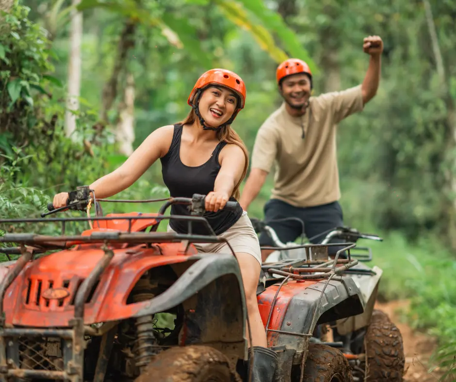 Couple riding muddy ATVs through a lush tropical trail during an off-road adventure in forest.