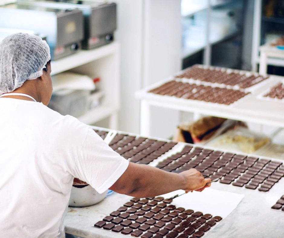 Worker arranging handmade chocolates on trays inside a chocolate factory in Barbados.