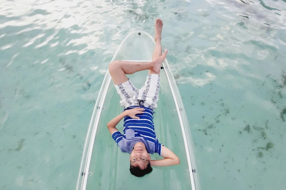 Person relaxing on a glass-bottom kayak floating over crystal-clear Caribbean water in Barbados.