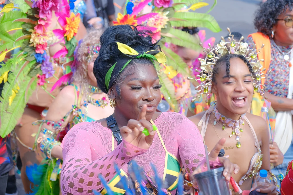 Two masqueraders in pink and gold costumes with floral headpieces laughing together in the crowd at Munich Carnival