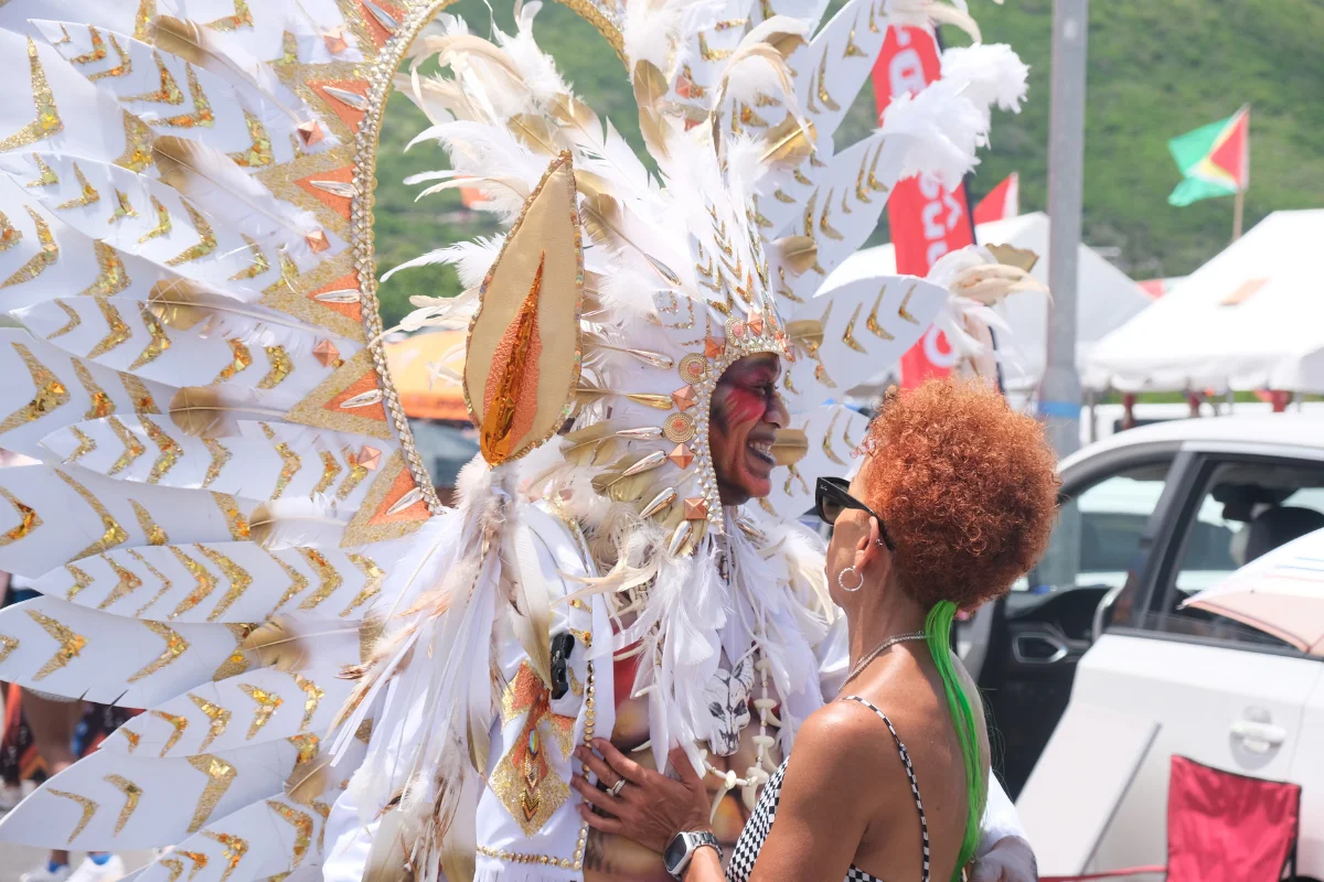 Masquerader in an elaborate white feathered carnival costume chatting with a spectator during Sint Maarten Carnival.