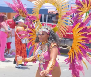 Smiling masquerader in a pink and gold costume with a sunburst headpiece and feather wings at SXM Carnival, one of the Caribbean Carnivals 2027