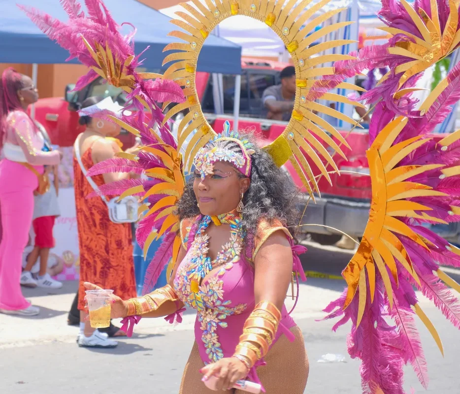 Smiling masquerader in a pink and gold costume with a sunburst headpiece and feather wings at SXM Carnival, one of the Caribbean Carnivals 2027