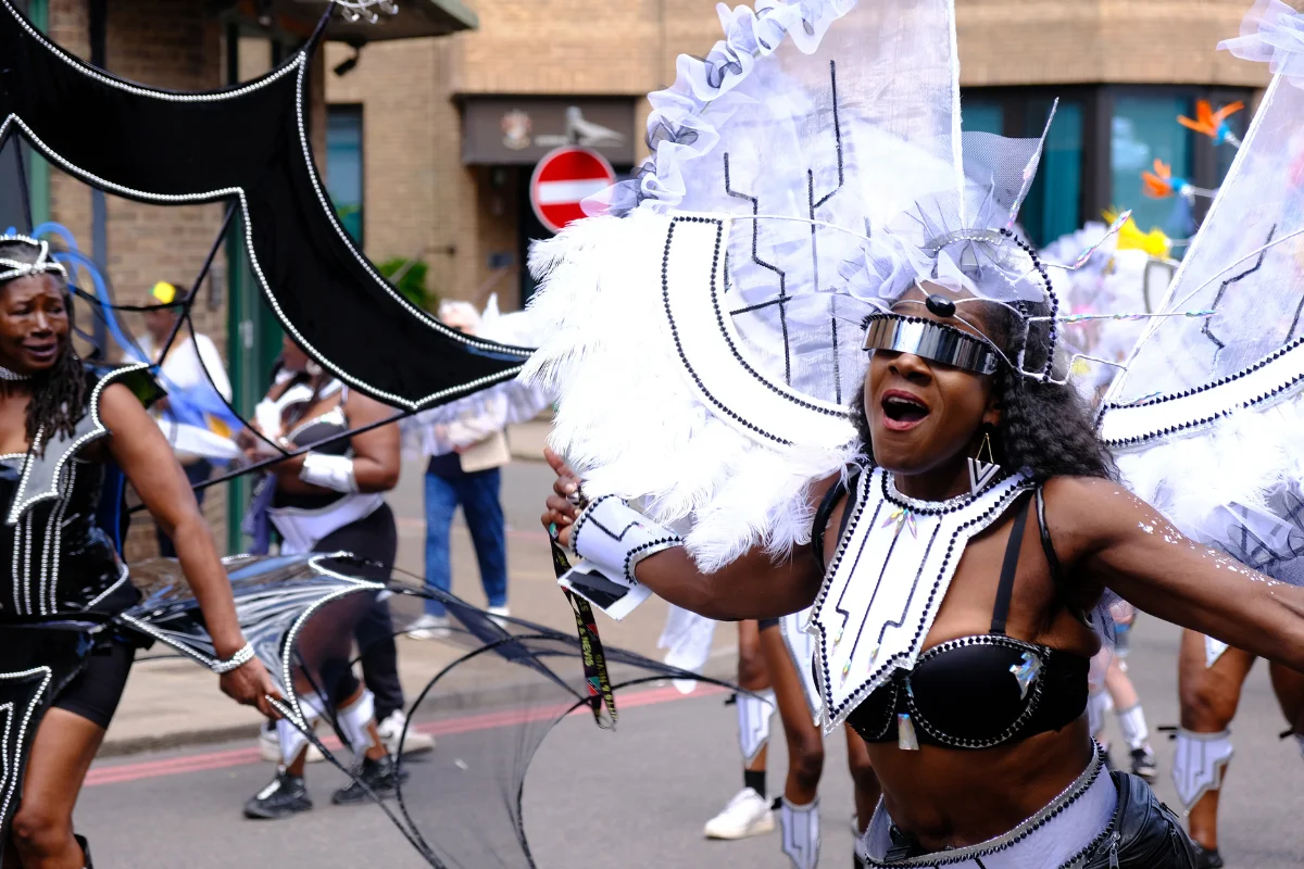 Masquerader in a white and black feathered costume with silver detailing dancing on the road at Luton Carnival
