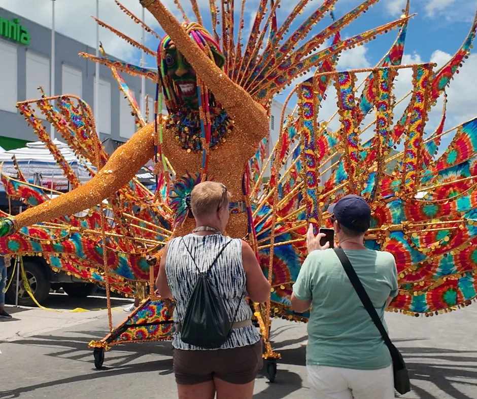 SXM Carnival spectator photographing a large orange, turquoise and multicolored carnival costume during the parade