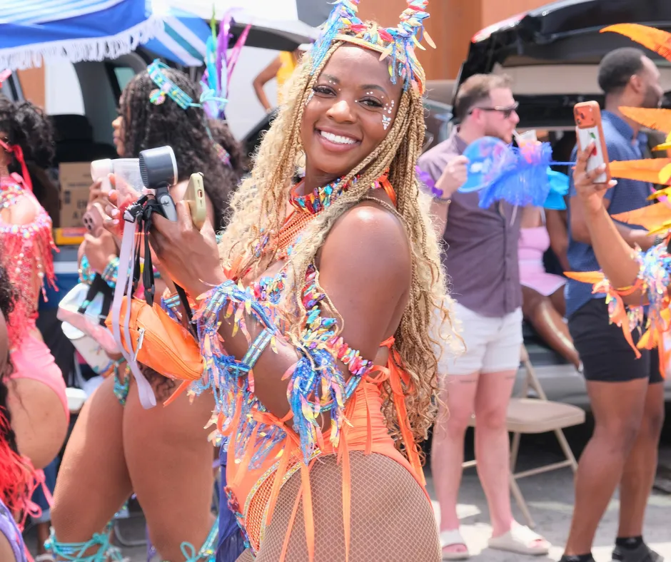 SXM Carnival masquerader smiling in a colorful orange and blue costume during the parade in Philipsburg