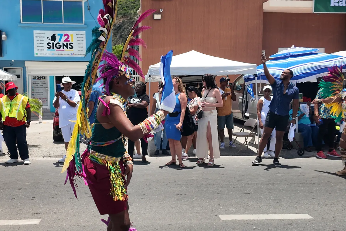 Spectator filming a colorful feathered masquerader during the daytime SXM Carnival parade in Philipsburg