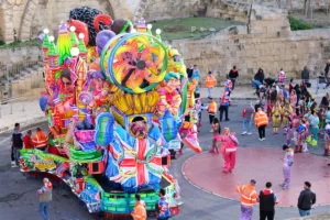 Towering mechanized carnival float covered in painted figures passing Valletta's limestone bastions during Carnival in Malta