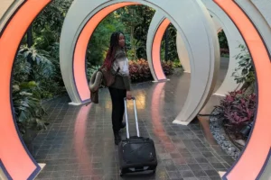 Shelley pulling suitcases through a busy airport terminal under gate signs