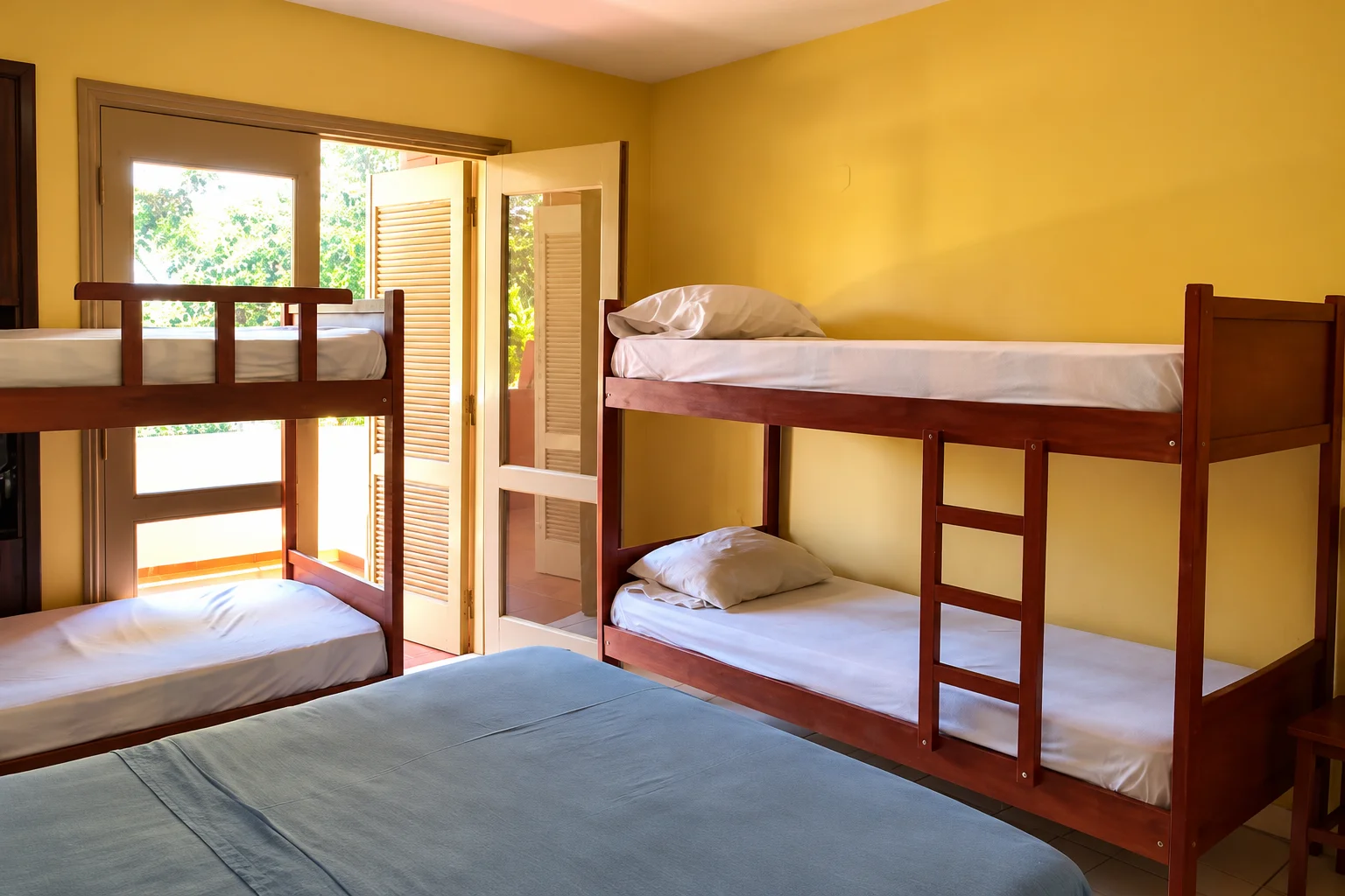 Wooden bunk beds in a yellow dorm room at La Casa de Pedro Hostel, opening onto a balcony