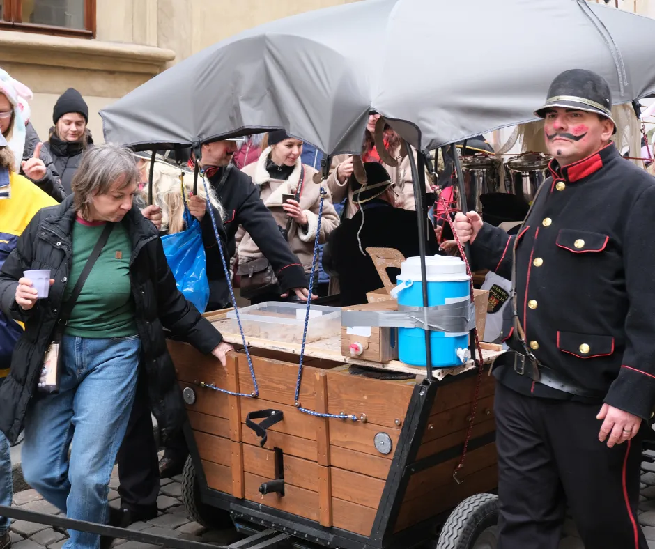 Masopust vendor in a traditional uniform serving warm drinks from a wooden cart in Prague during the winter carnival