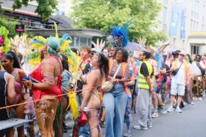 Carnival participants in white and light blue traditional outfits parade through a crowded Munich street as spectators gather along the route