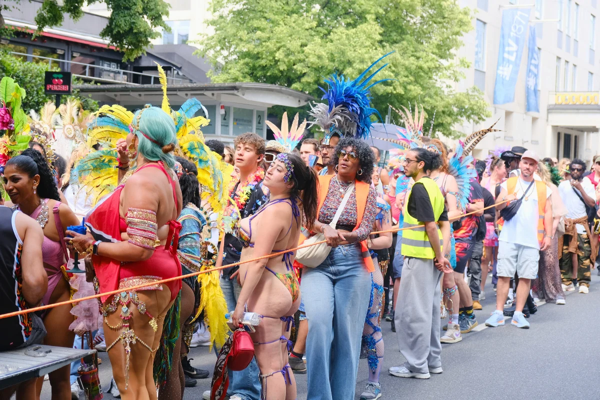Carnival participants in white and light blue traditional outfits parade through a crowded Munich street as spectators gather along the route