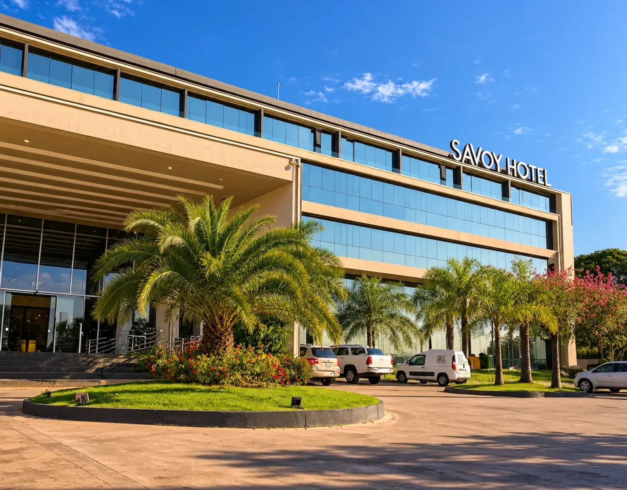 Savoy Hotel exterior featuring modern glass windows palm trees and a landscaped entrance beneath a clear blue sky