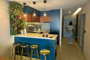 Modern vacation rental kitchen with blue cabinets, gold bar stools, and a living plant wall, representing rental options for travelers deciding where to stay for Carnival 2027.