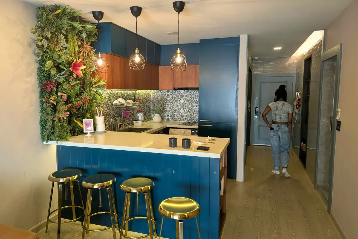 Modern vacation rental kitchen with blue cabinets, gold bar stools, and a living plant wall, representing rental options for travelers deciding where to stay for Carnival 2027.