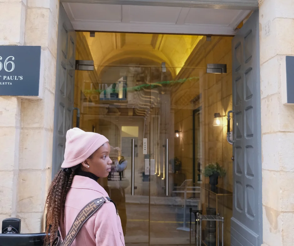 Traveller in a pink coat and beanie outside the entrance to 66 Saint Paul's, one of the mid-range hotels for Malta Carnival in Valletta